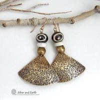 These handcrafted earrings feature gold brass fan-shaped dangles with a rustic hammered texture accented with African batik bone beads, off-white magnesite stones and African brass beads. Unique and striking, they have a bold ethnic vibe with African tribal flair that makes a striking statement. Handmade in the USA by Silver and Earth Jewelry. 