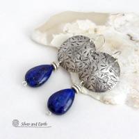These earrings feature teardrop-shaped natural blue lapis lazuli gemstones dangling from handcrafted sterling silver with a hand stamped texture. The stones are a rich shade of blue and are topped off with silver pewter beads. They have a contemporary, modern chic style that makes a bold statement.