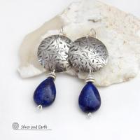 These earrings feature teardrop-shaped natural blue lapis lazuli gemstones dangling from handcrafted sterling silver with a hand stamped texture. The stones are a rich shade of blue and are topped off with silver pewter beads. They have a contemporary, modern chic style that makes a bold statement.