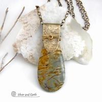 This handcrafted necklace features a natural Picasso jasper gemstone accented with a gold brass bail. The stone has a beautiful matrix with earthy hues of soft yellow, light mossy green and brown streaks. It has an earthy, modern style that coordinates beautifully with all wardrobe types. Unique and one of a kind, it makes a great gift for a natural stone lover - or a nice addition to your own jewelry collection. Comes on a 20" antiqued brass chain with lobster claw closure.  