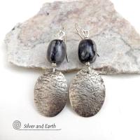 These handcrafted earrings feature sterling silver oval dangles accented with Picasso marble gemstones. This semiprecious stone is found only in southwest Utah. It's named after the famous artist because the natural matrix of geometric lines resembles an abstract painting. The stones in this pair have distinctive swirly lines in black and grey. They have a modern, earthy style and are lightweight and comfortable to wear.