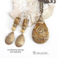 This one-of-a-kind necklace features a natural picture jasper stone wrapped in gold brass wire. The stone has an interesting matrix pattern with earthy hues of brown, tan and black. It has an earthy, simple style that coordinates beautifully with all wardrobe styles. It makes a great gift for a natural stone lover - or a nice addition to your own jewelry collection. Handmade in the USA by Silver and Earth Jewelry. Coordinating earrings sold separately.