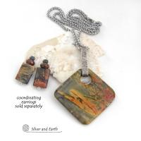 This one-of-a-kind necklace features a natural red creek jasper stone accented with a hand forged sterling silver bail. The stone has a beautiful natural pattern in earthy hues of mossy greens, brick red and orange. Coordinating earrings sold separately. 