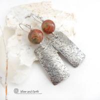 These sterling silver earrings have a modern, earthy organic flair. They feature handcrafted sterling silver rectangles with a rustic hammered texture accented with natural red creek jasper stones. The stones have a beautiful natural pattern in earthy hues of mossy greens, brick red and orange. 