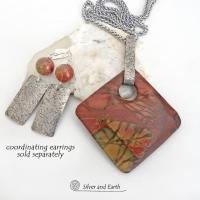 This one-of-a-kind necklace features a natural red creek jasper stone accented with a hand forged sterling silver bail with a lightly hammered texture. The stone has a beautiful natural pattern in earthy hues of mossy greens, brick red, brown and orange. It's reversible and can be worn on either side. It makes a great gift for anyone that loves earthy colors and natural stones. The design is unisex so it could be worn by a man or woman. Coordinating earrings sold separately. 