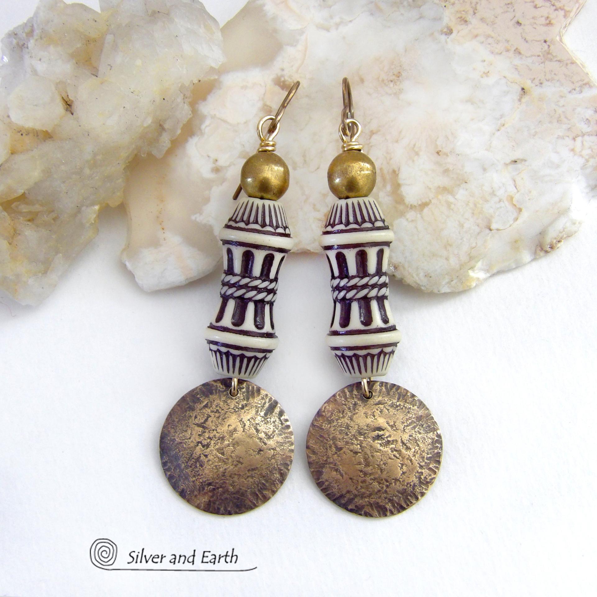 Bold and unique, these handcrafted earrings have an ethnic African tribal vibe. They feature gold brass dangles with a hammered rustic texture accented with exotic African beads with an intricate brown and white carved pattern topped off with gold brass beads. Unique and fun to wear - they'll make a bold, striking statement. Perfect for women that love to wear one-of-a-kind artisan handcrafted jewelry. Handmade in the USA by Silver and Earth Jewelry. 