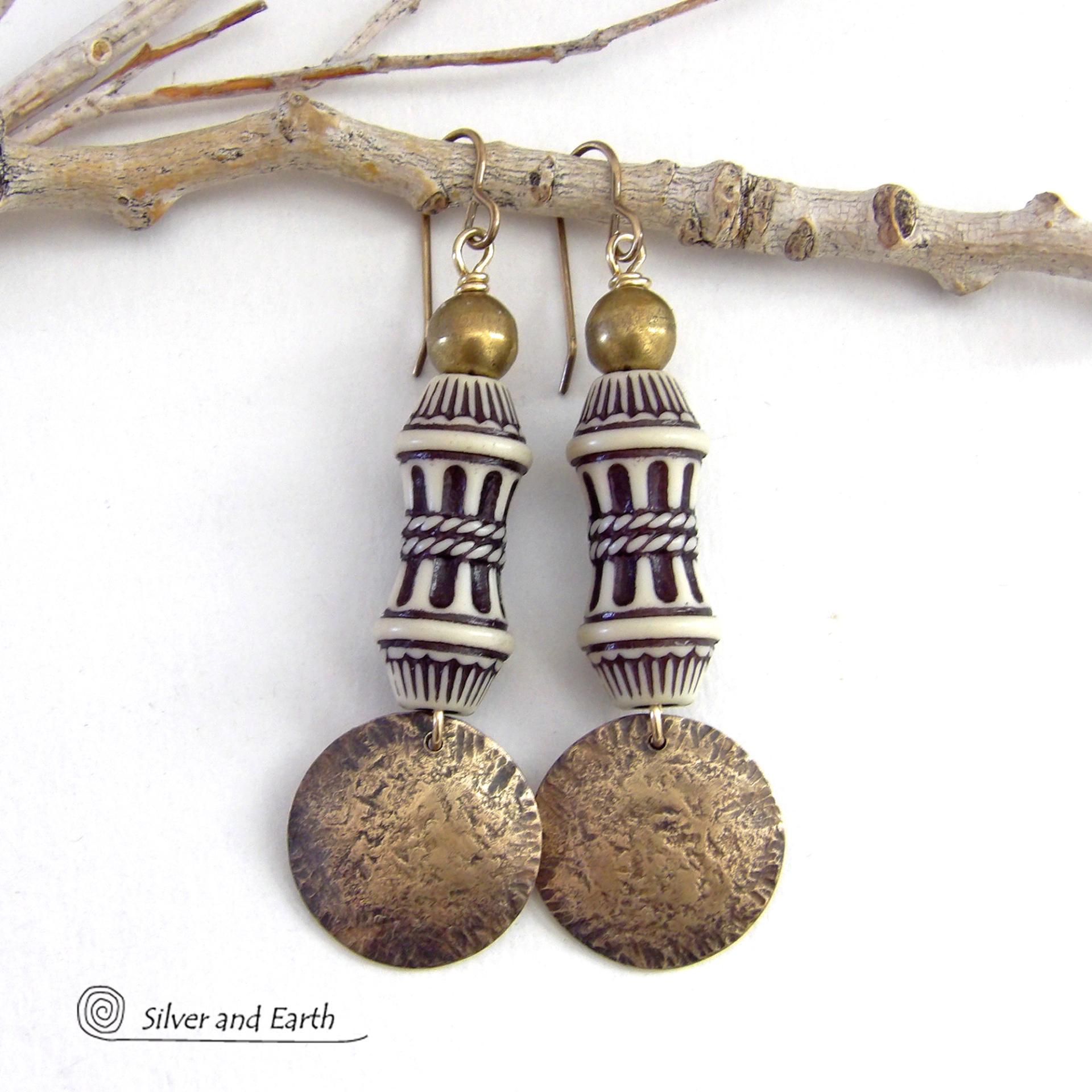 Bold and unique, these handcrafted earrings have an ethnic African tribal vibe. They feature gold brass dangles with a hammered rustic texture accented with exotic African beads with an intricate brown and white carved pattern topped off with gold brass beads. Unique and fun to wear - they'll make a bold, striking statement. Perfect for women that love to wear one-of-a-kind artisan handcrafted jewelry. Handmade in the USA by Silver and Earth Jewelry. 