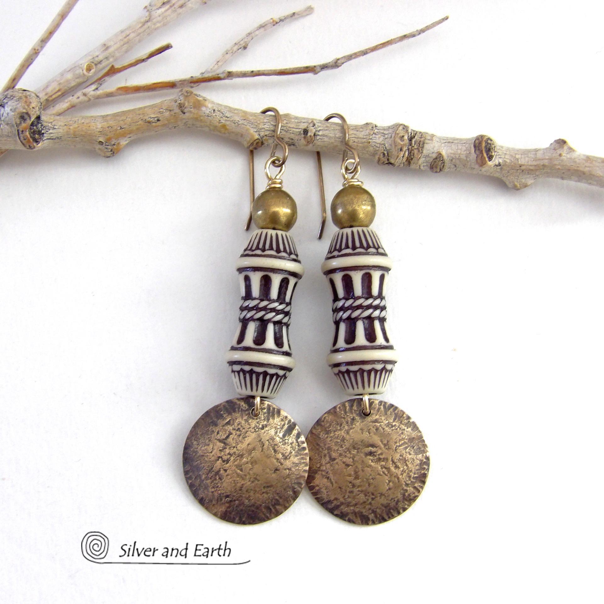 Bold and unique, these handcrafted earrings have an ethnic African tribal vibe. They feature gold brass dangles with a hammered rustic texture accented with exotic African beads with an intricate brown and white carved pattern topped off with gold brass beads. Unique and fun to wear - they'll make a bold, striking statement. Perfect for women that love to wear one-of-a-kind artisan handcrafted jewelry. Handmade in the USA by Silver and Earth Jewelry. 