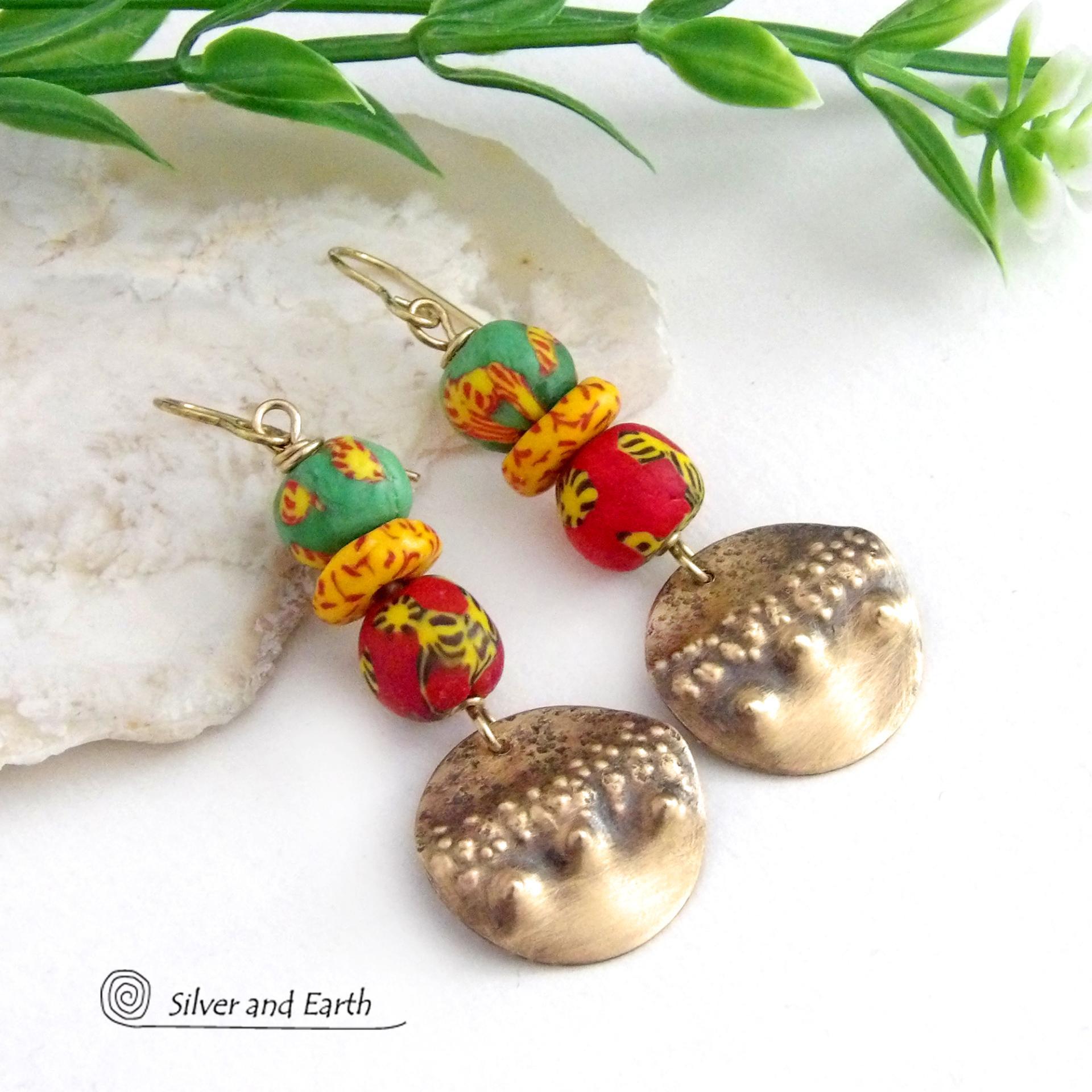 Bold and unique - these gold brass dangle earrings will surely brighten your day! They feature bright and colorful African glass beads with beautiful hues of green, red and yellow. They are accented with handcrafted gold brass dangles with a hammered organic texture. The African beads are handcrafted by artisans in Ghana from recycled glass by a traditional process passed down thru many generations. These earrings have a bohemian Afrocentric style with lots of fashionable flair! 