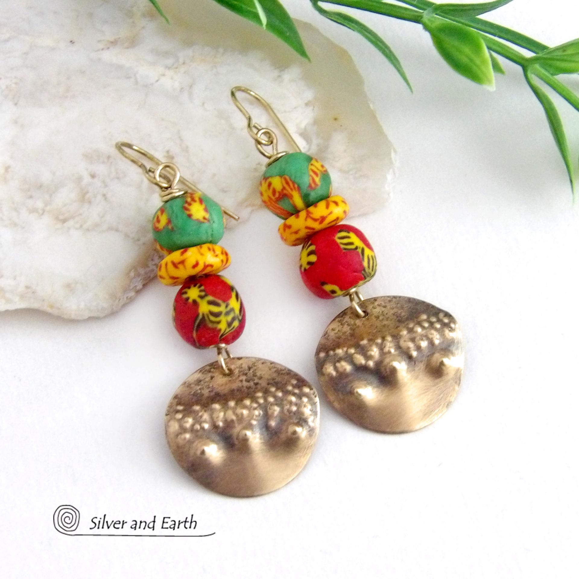 Bold and unique - these gold brass dangle earrings will surely brighten your day! They feature bright and colorful African glass beads with beautiful hues of green, red and yellow. They are accented with handcrafted gold brass dangles with a hammered organic texture. The African beads are handcrafted by artisans in Ghana from recycled glass by a traditional process passed down thru many generations. These earrings have a bohemian Afrocentric style with lots of fashionable flair! 