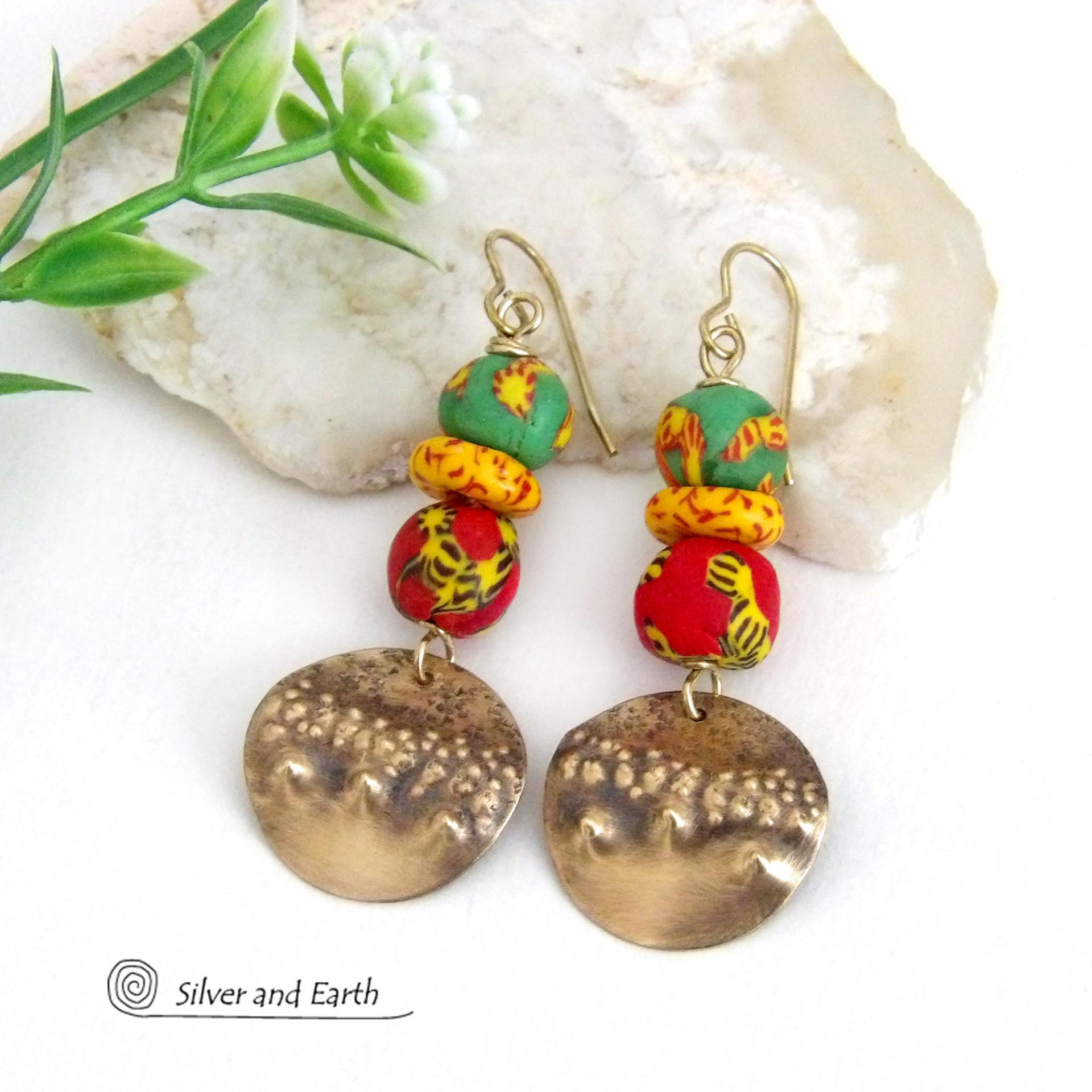 Bold and unique - these gold brass dangle earrings will surely brighten your day! They feature bright and colorful African glass beads with beautiful hues of green, red and yellow. They are accented with handcrafted gold brass dangles with a hammered organic texture. The African beads are handcrafted by artisans in Ghana from recycled glass by a traditional process passed down thru many generations. These earrings have a bohemian Afrocentric style with lots of fashionable flair! 
