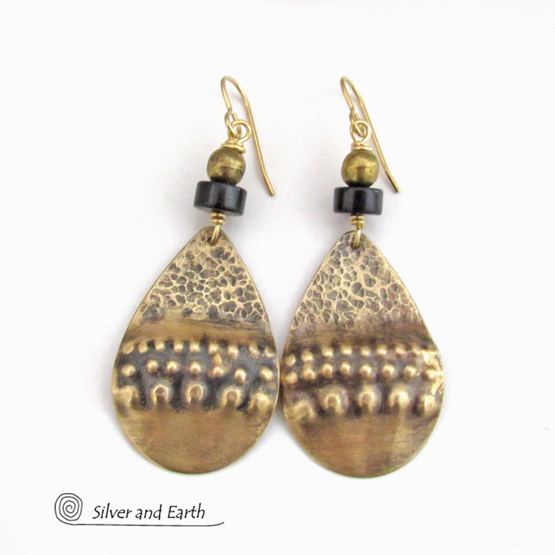 These handcrafted earrings feature textured gold brass teardrop dangles accented with matte black jasper stones and brass beads. They have an exotic, boho tribal vibe that makes a bold statement. 