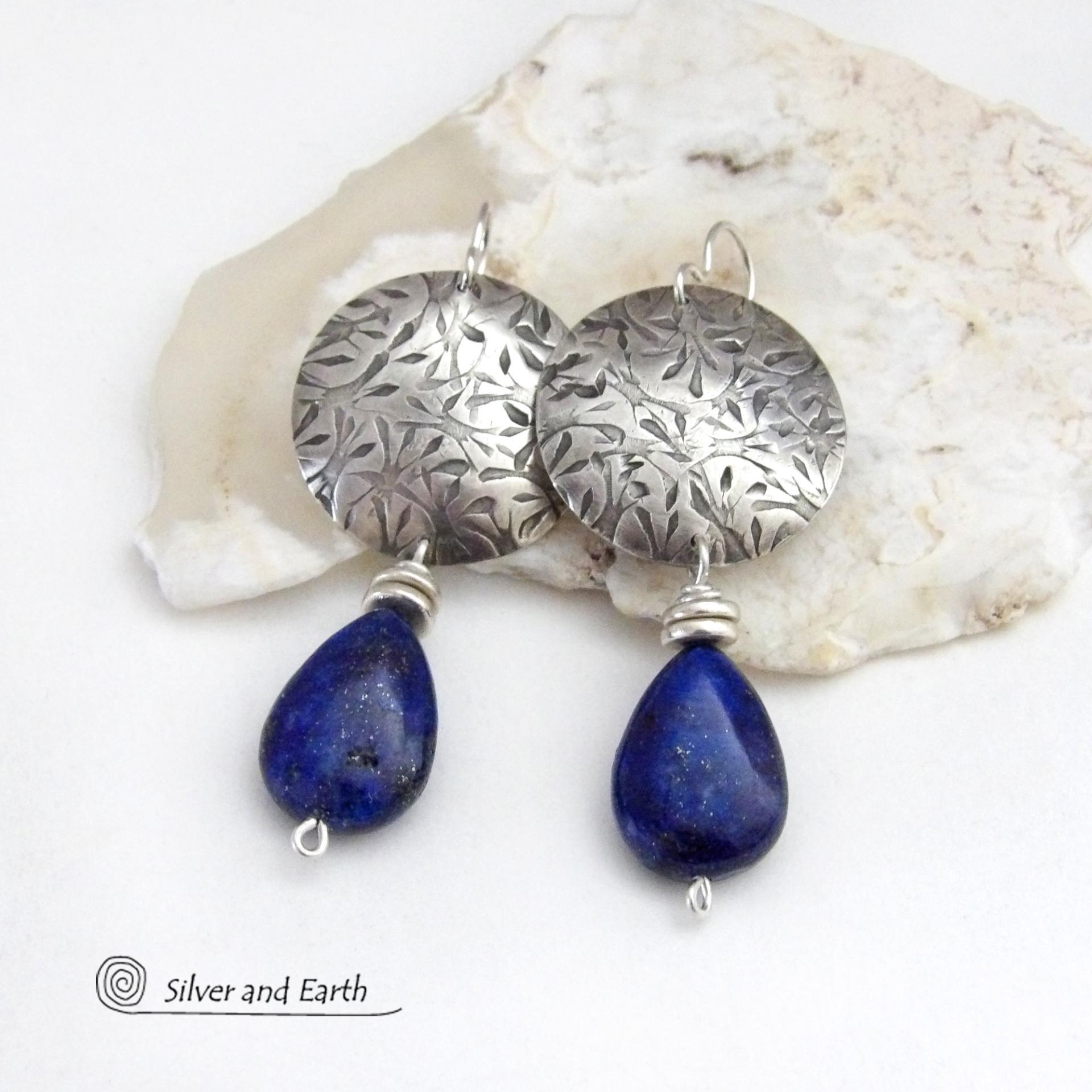 These earrings feature teardrop-shaped natural blue lapis lazuli gemstones dangling from handcrafted sterling silver with a hand stamped texture. The stones are a rich shade of blue and are topped off with silver pewter beads. They have a contemporary, modern chic style that makes a bold statement.