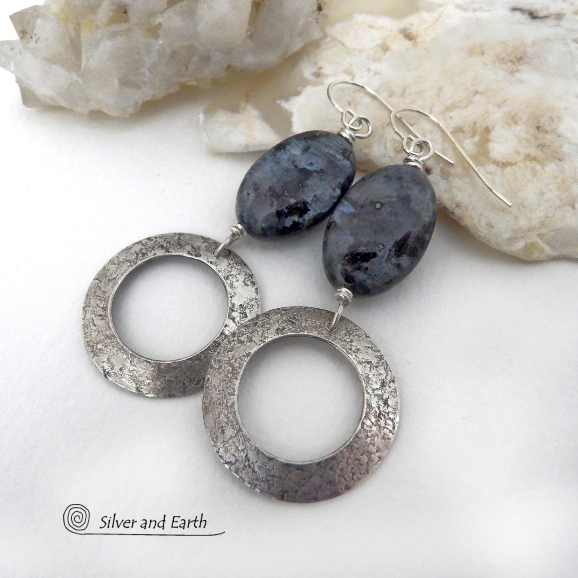 These handcrafted earrings feature natural larvikite gemstones accented with sterling silver hoop dangles with a lightly hammered texture. The stones have a pearly, grayish black hue - along with blue iridescent flashes of light which cast off a natural shimmer & shine. Perfect "go to" earrings that will look great with all wardrobe styles - dressed up or down! Larvikite originates from the Larvik region in Norway and is also called Norwegian moonstone and black labradorite. 