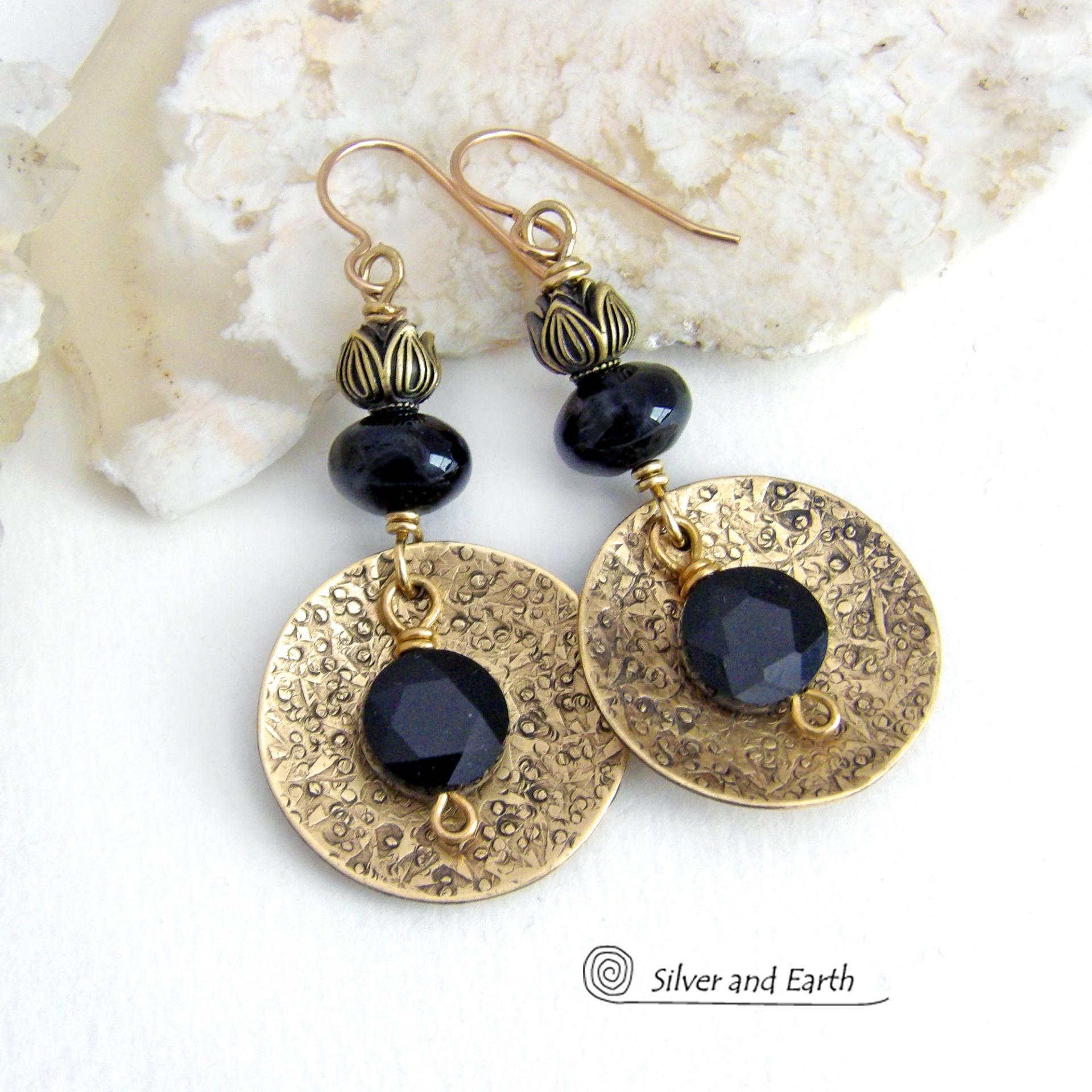 These handcrafted earrings feature gold brass dangles with a hand stamped texture accented with round black onyx gemstones dangling in front and topped off with black onyx gemstones and tulip flower-shaped beads. The round onyx stones have a faceted cut which casts off a beautiful natural sparkle and shine. They have a modern, elegant chic style that looks great dressed up or down. Perfect for women that love bold unique artisan handcrafted jewelry. Handmade in the USA by Silver and Earth Jewelry.