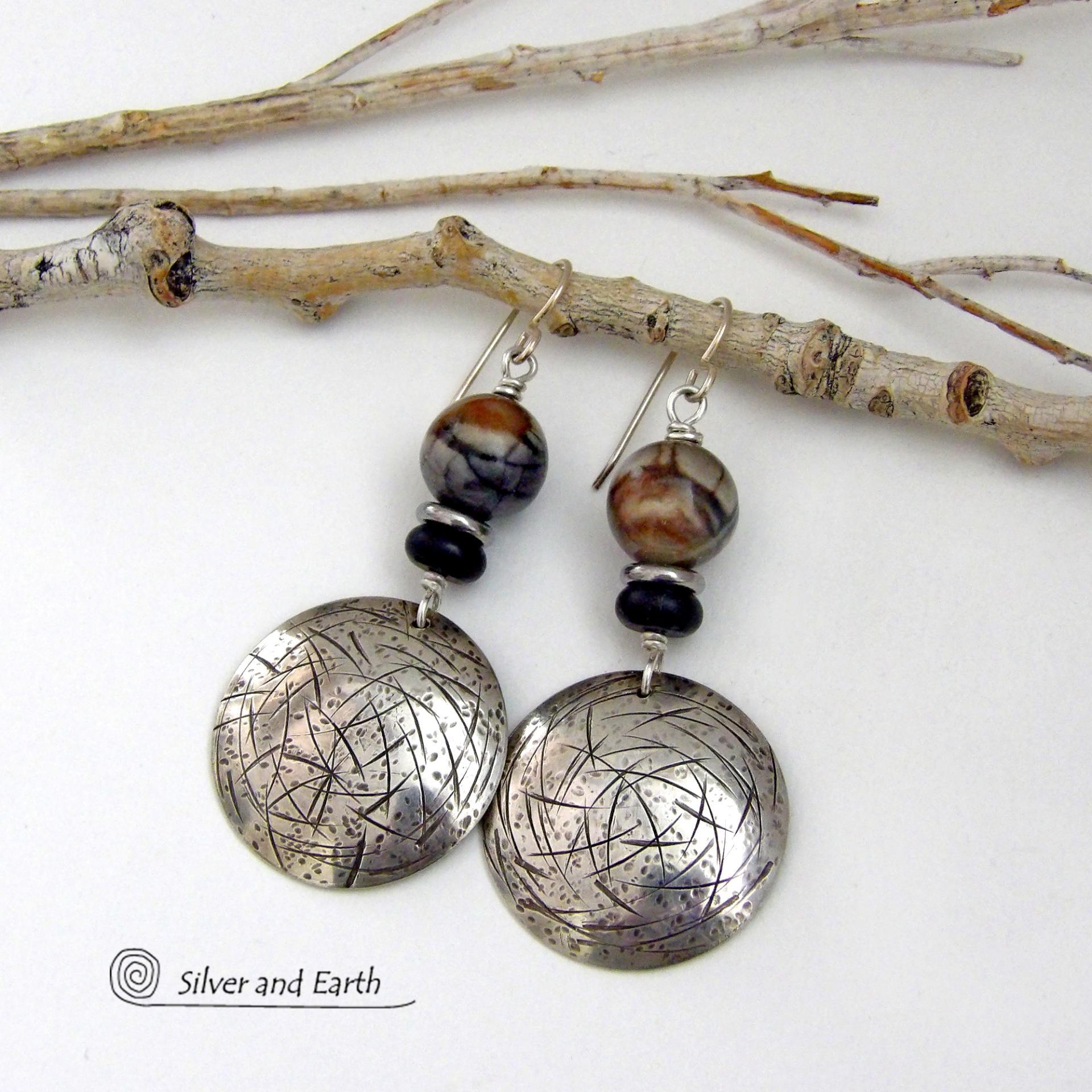 These one-of-a-kind earrings feature handcrafted sterling silver with a hammered and hand stamped texture accented with earthy natural Picasso marble gemstones, black glass and stainless steel beads. This semiprecious stone is found only in southwest Utah. It's named after the famous artist because the natural matrix of geometric lines resembles an abstract painting. The stones in this pair have a beautiful matrix pattern of distinctive swirly lines in black, grey and chocolate brown.