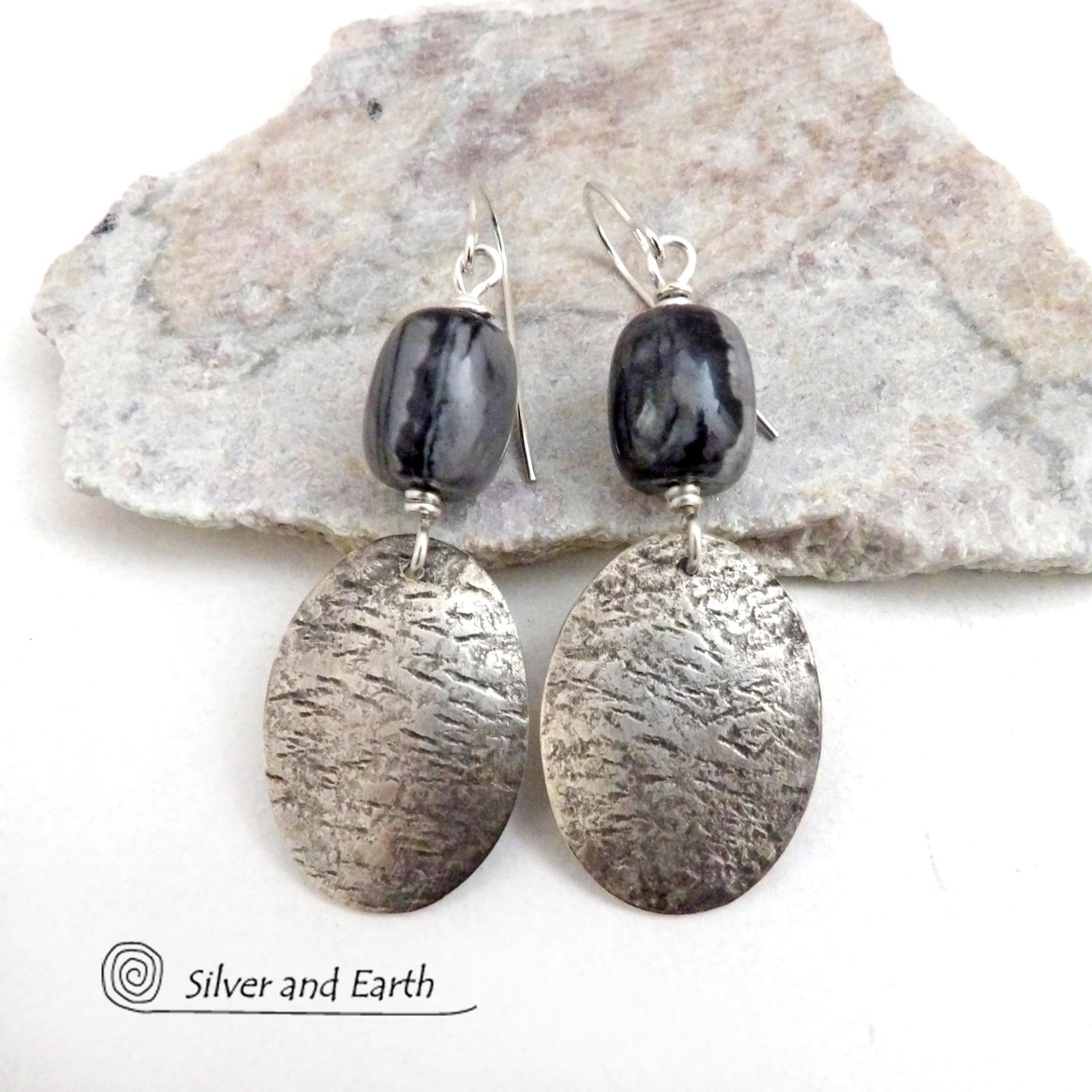 These handcrafted earrings feature sterling silver oval dangles accented with Picasso marble gemstones. This semiprecious stone is found only in southwest Utah. It's named after the famous artist because the natural matrix of geometric lines resembles an abstract painting. The stones in this pair have distinctive swirly lines in black and grey. They have a modern, earthy style and are lightweight and comfortable to wear.