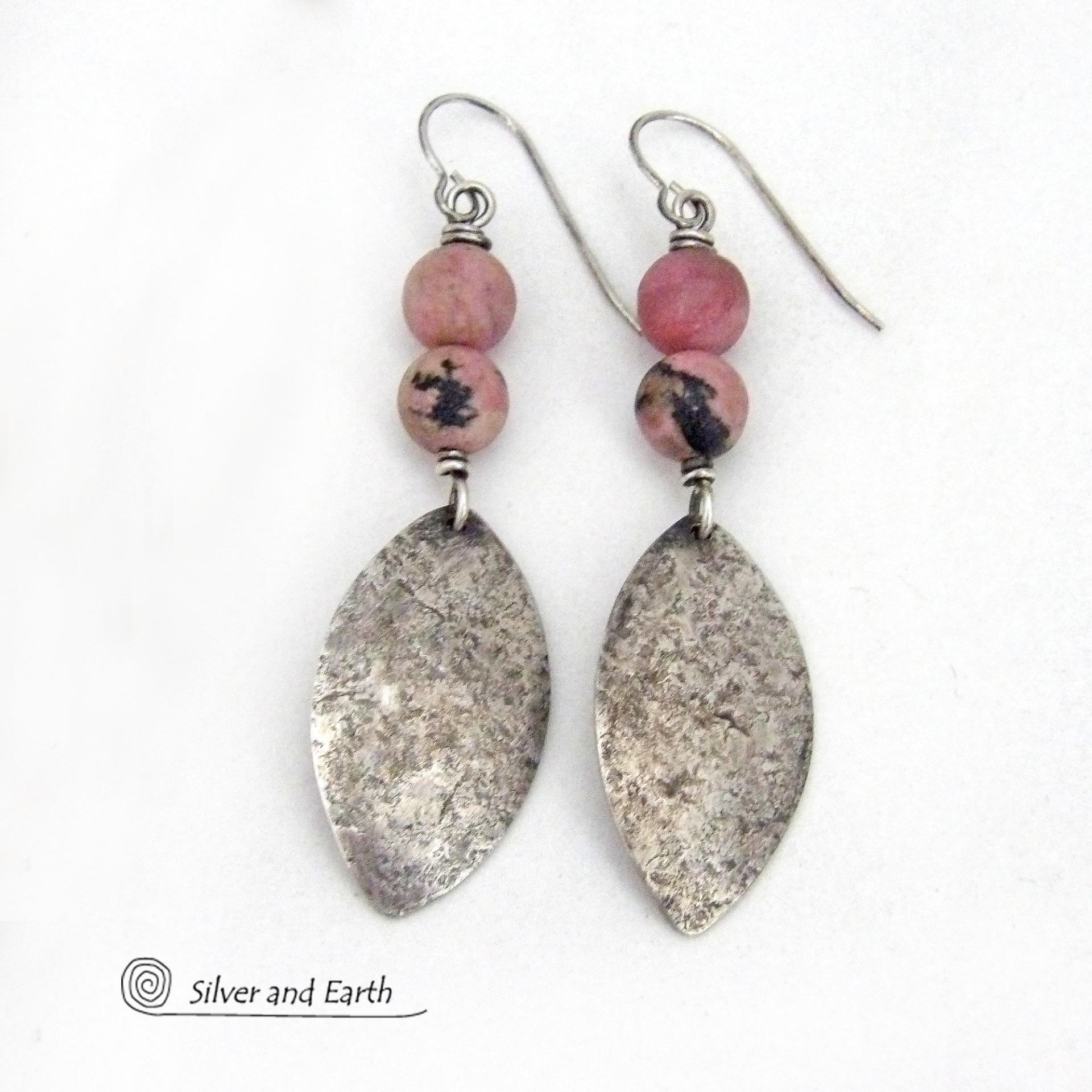 These sterling silver dangle earrings have a rustic lightly hammered texture and are accented with a stack of pink rhodonite gemstones. The stones have a pretty pink hue with a natural black spot matrix. They have a modern, contemporary style that coordinates well with all wardrobe types. 