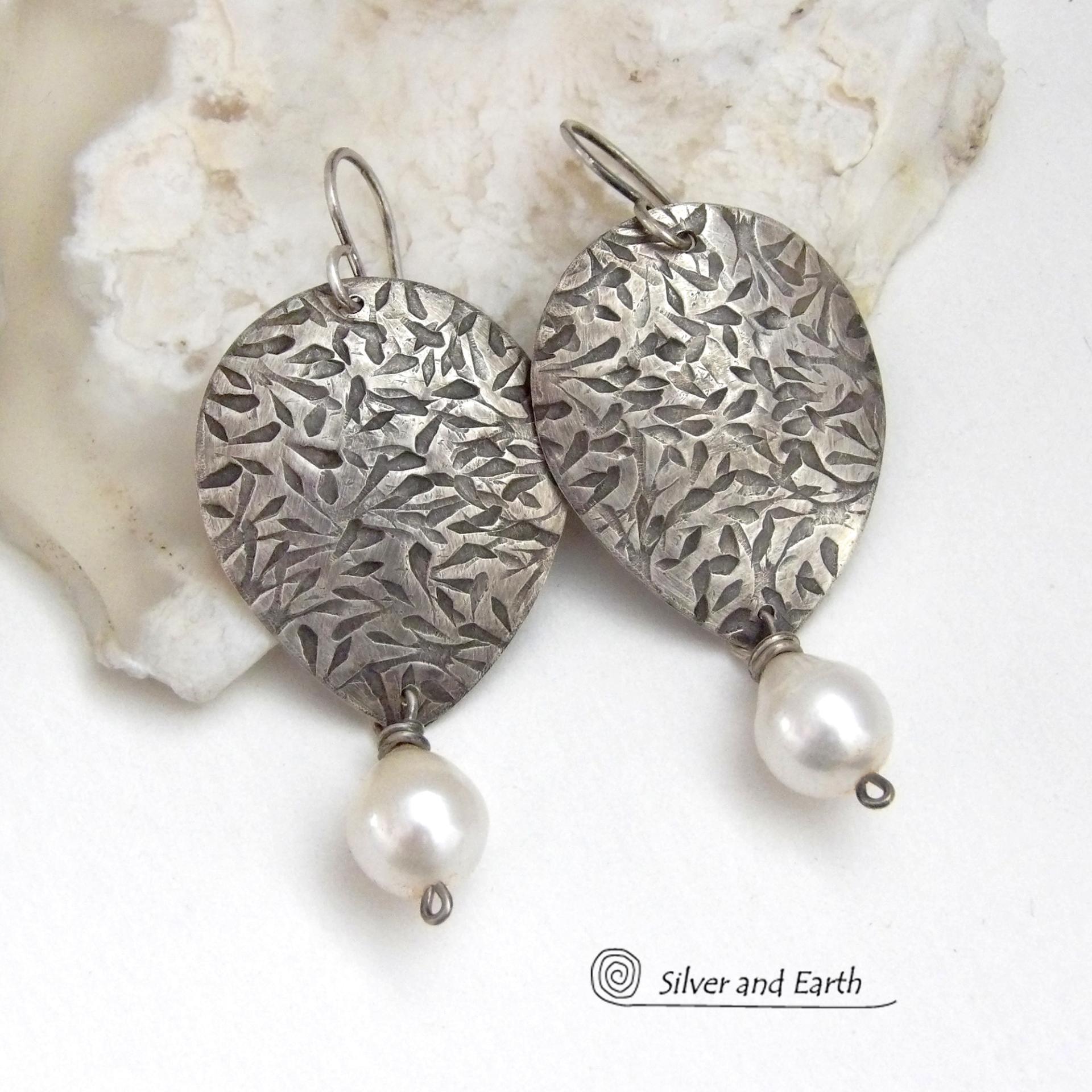 Perfect for everyday wear, these handcrafted sterling silver earrings are accented with dangling white freshwater pearls. The silver has an intricate hand stamped texture with an oxidized finish. The pearls contrast beautifully against the silver metal. They have an elegant, feminine feel with a contemporary design that looks great with all wardrobe styles. They'll make a great gift for someone born in June. Pearl is the traditional gemstone for this month. Handmade in the USA by Silver and Earth Jewelry. 