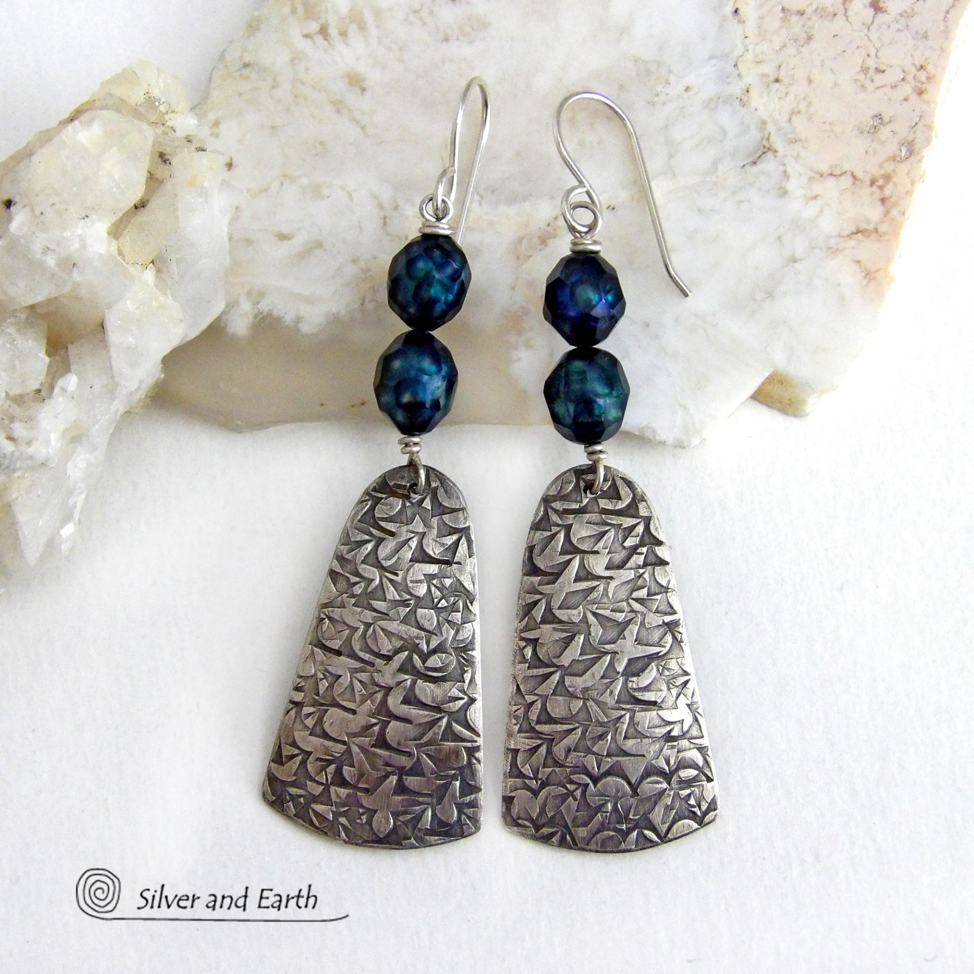 These sterling silver earrings feature handcrafted sterling silver dangles with an intricate hand stamped texture accented with deep teal blue freshwater pearls with a faceted finish.  They have a modern, elegant feel and will look great dressed up or down. They dangle from sterling silver ear wires. Handmade in the USA by Silver and Earth Jewelry. 